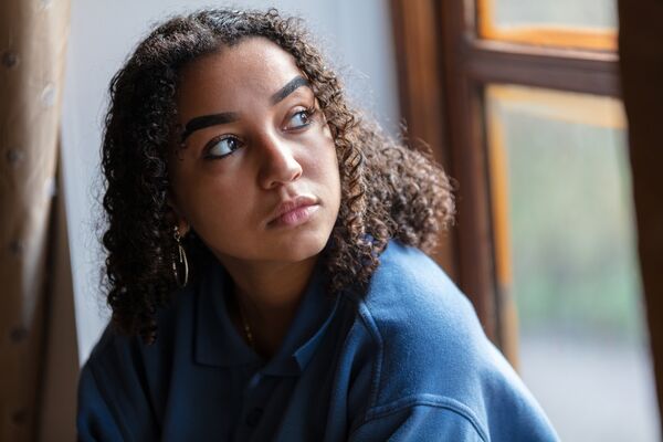 Beautiful mixed race African American girl teenager female young woman sad depressed or worried looking out of a window